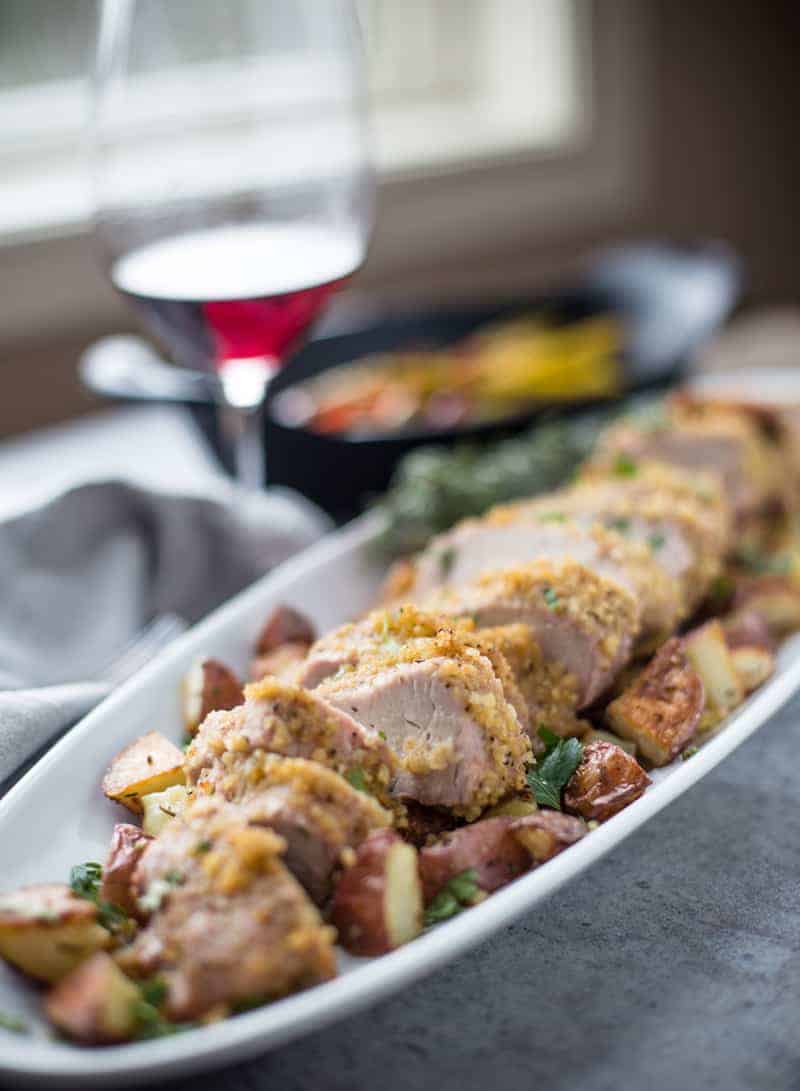 Slices of pork on a long platter with potatoes and a glass of wine