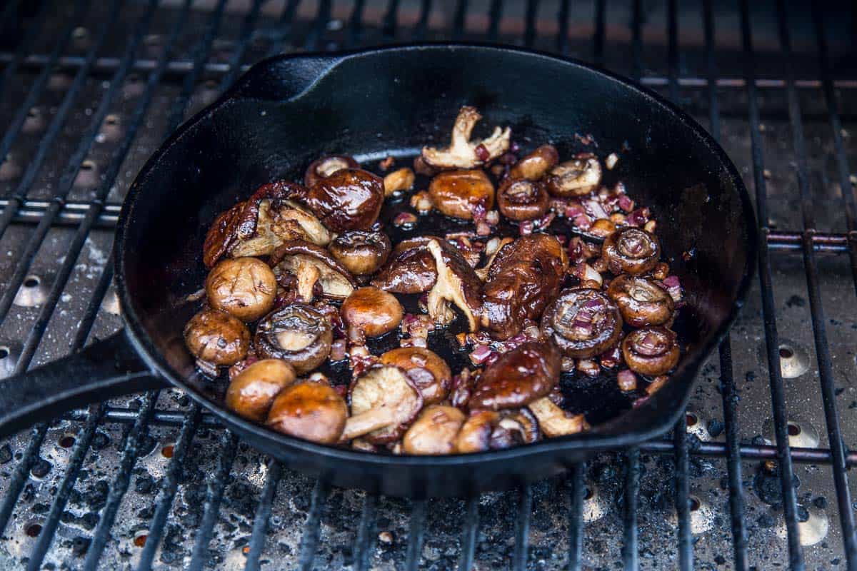 Mushrooms cooking in a cast iron pan on a grill