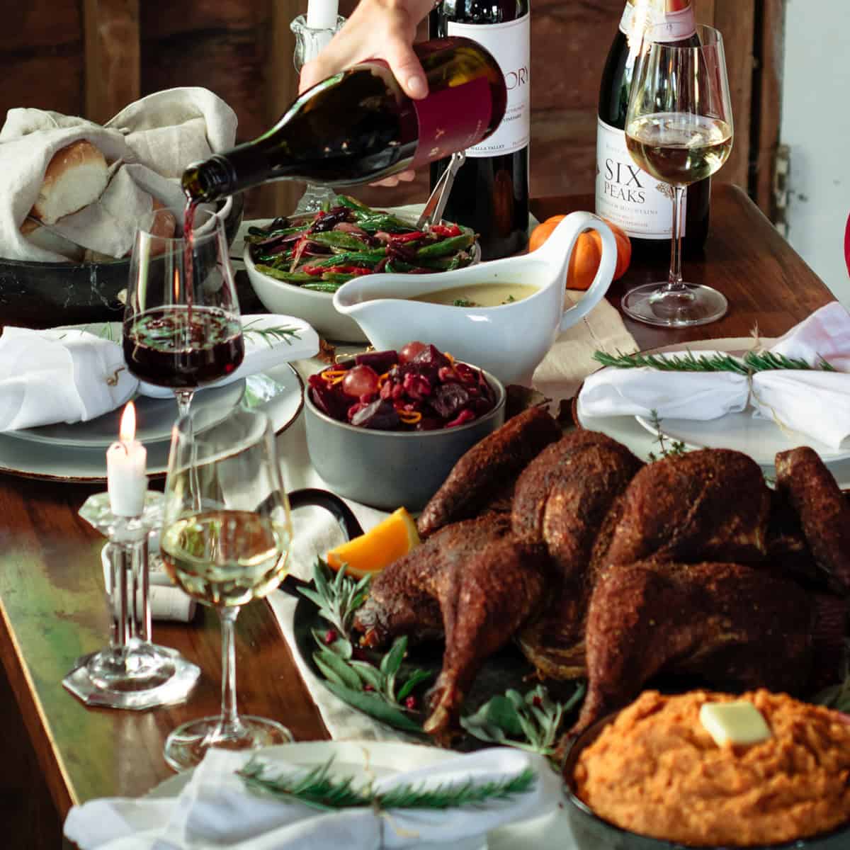 Holiday spread with a smoked turkey and a hand pouring wine into a wine glass