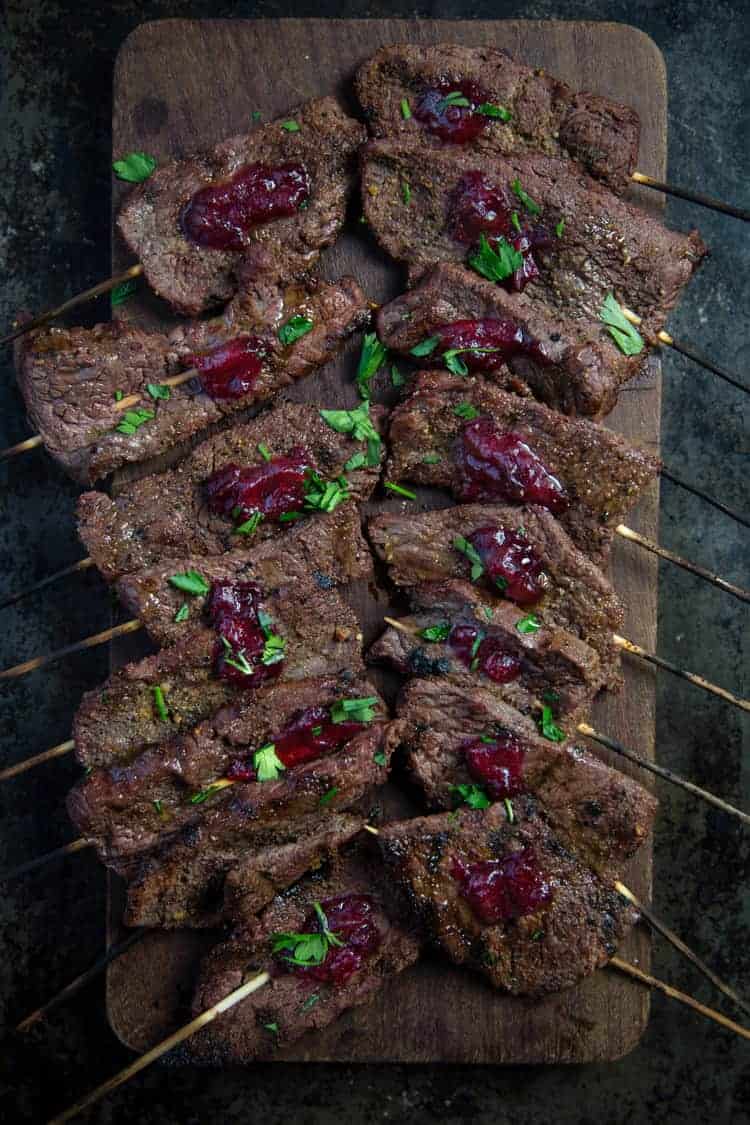 Beef skewers on a cutting board with cranberry relish.