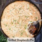 A grilled Shepherd's Pie with browned mashed potatoes and a spoon that has removed a small portion from the pie showing the minced meat filling.