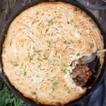 A grilled Shepherd's Pie with browned mashed potatoes and a spoon that has removed a small portion from the pie showing the minced meat filling.