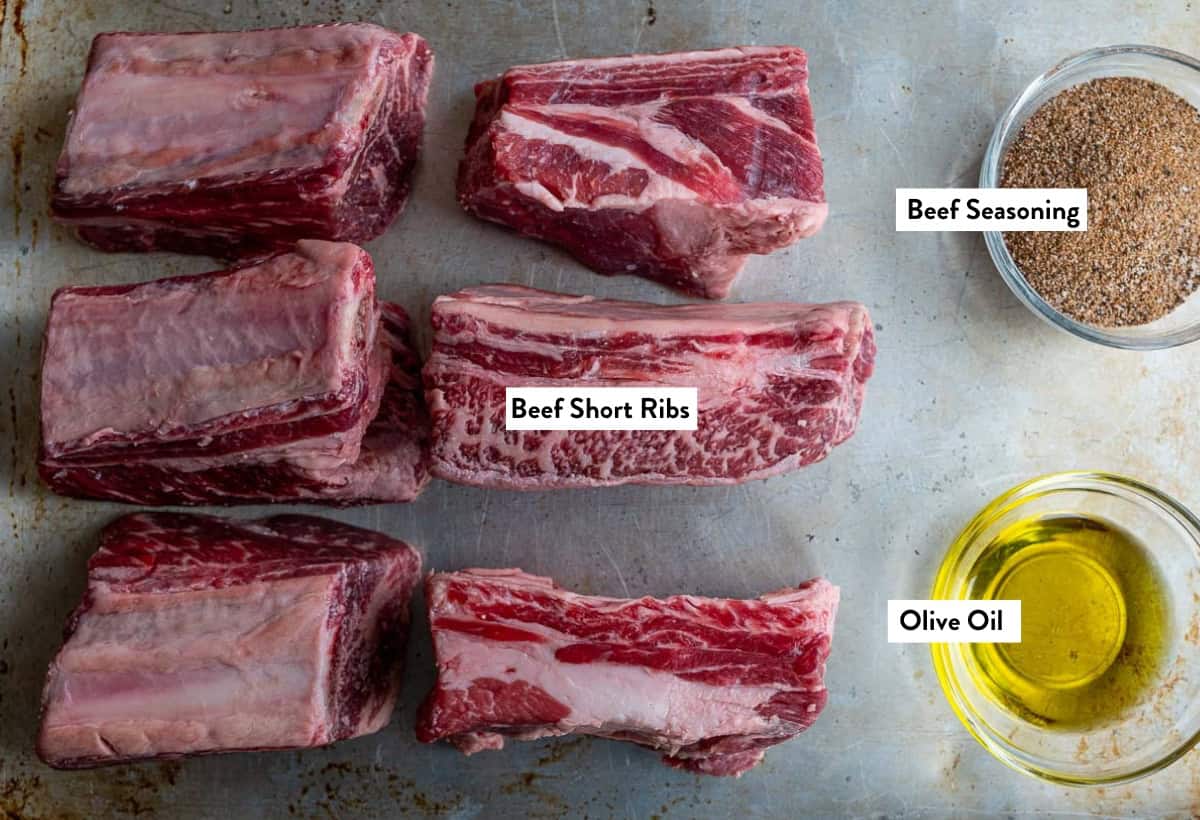 Ingredient photo of smoked beef short ribs, olive oil, and beef seasoning on sheet tray before being seasoned.