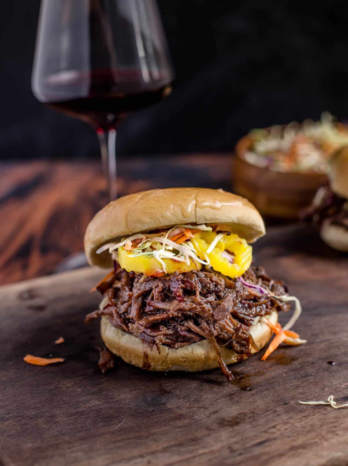 Smoked Pulled Beef Sandwich on a cutting board with a glass of wine
