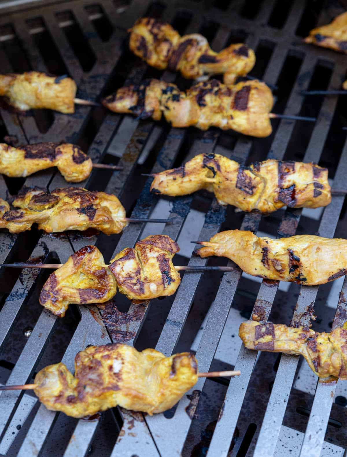 Chicken skewers on a gas grill grate over direct heat.