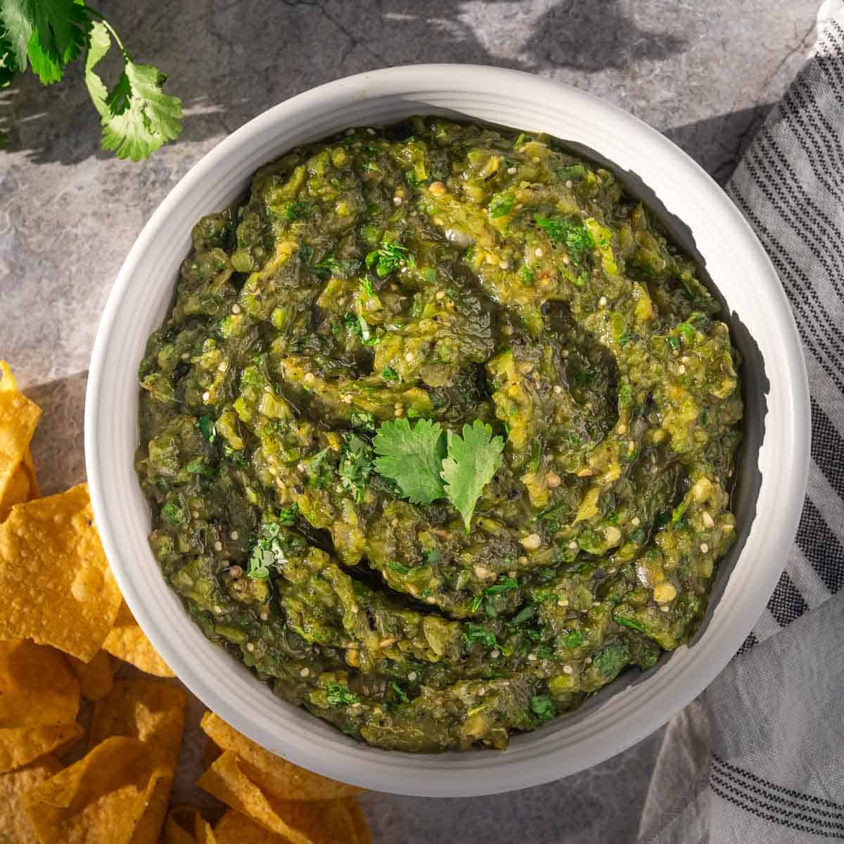 Square image of Hatch green chile salsa in a bowl surrounded by tortilla chips.