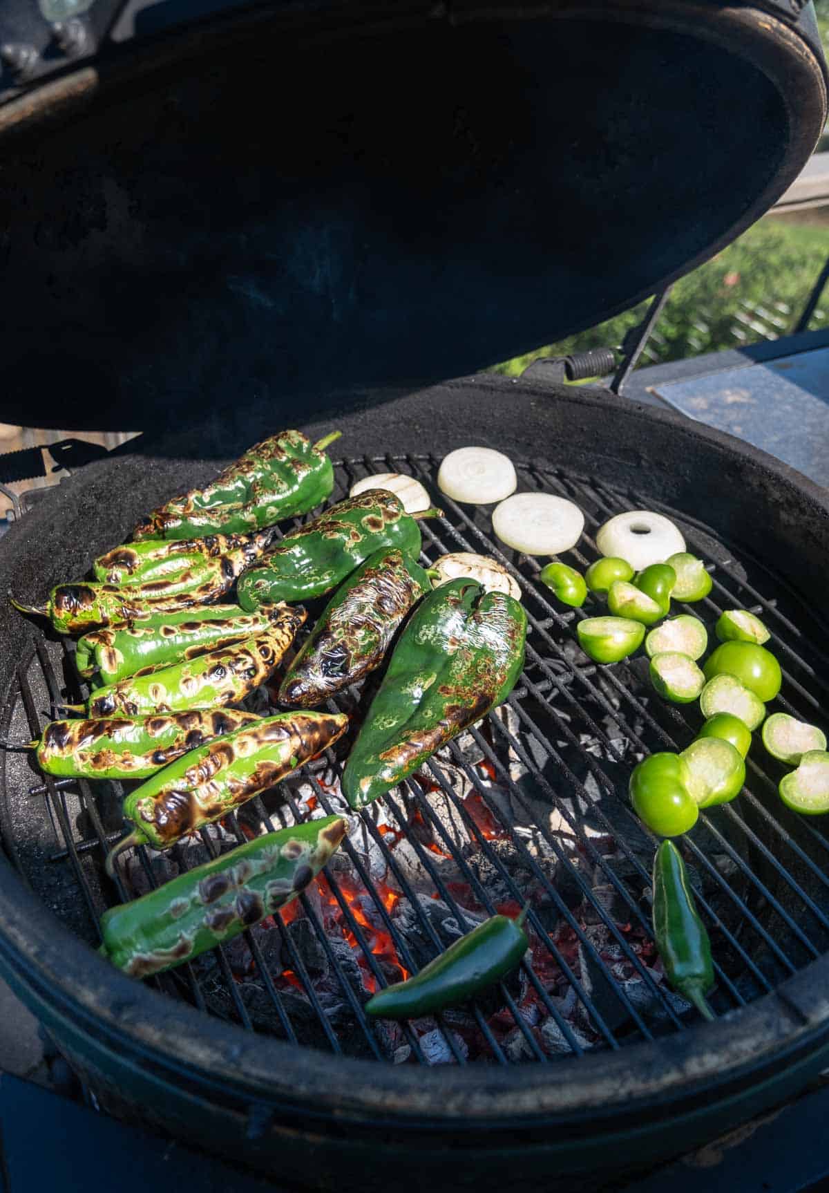 Ingredients over direct heat on a big green egg for green chile salsa including peppers and onions.