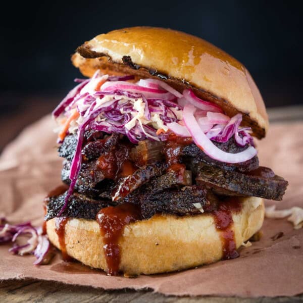 A BBQ Brisket Sandwich on a serving platter topped with homemade coleslaw and bbq sauce