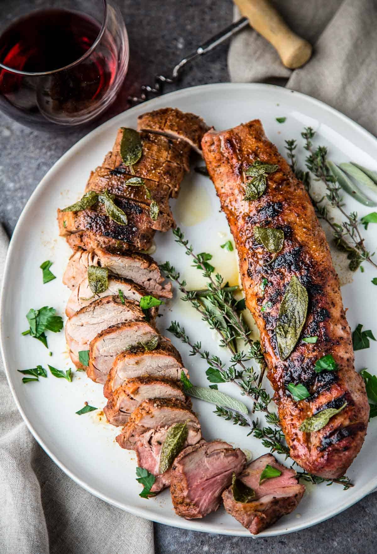 Grilled Pork Tenderloin topped with fried sage butter sauce on a platter with a glass of red wine