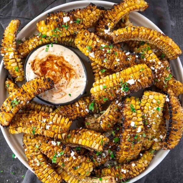 Corn Ribs with dipping sauce sitting in a plate sprinkled with cotija cheese.