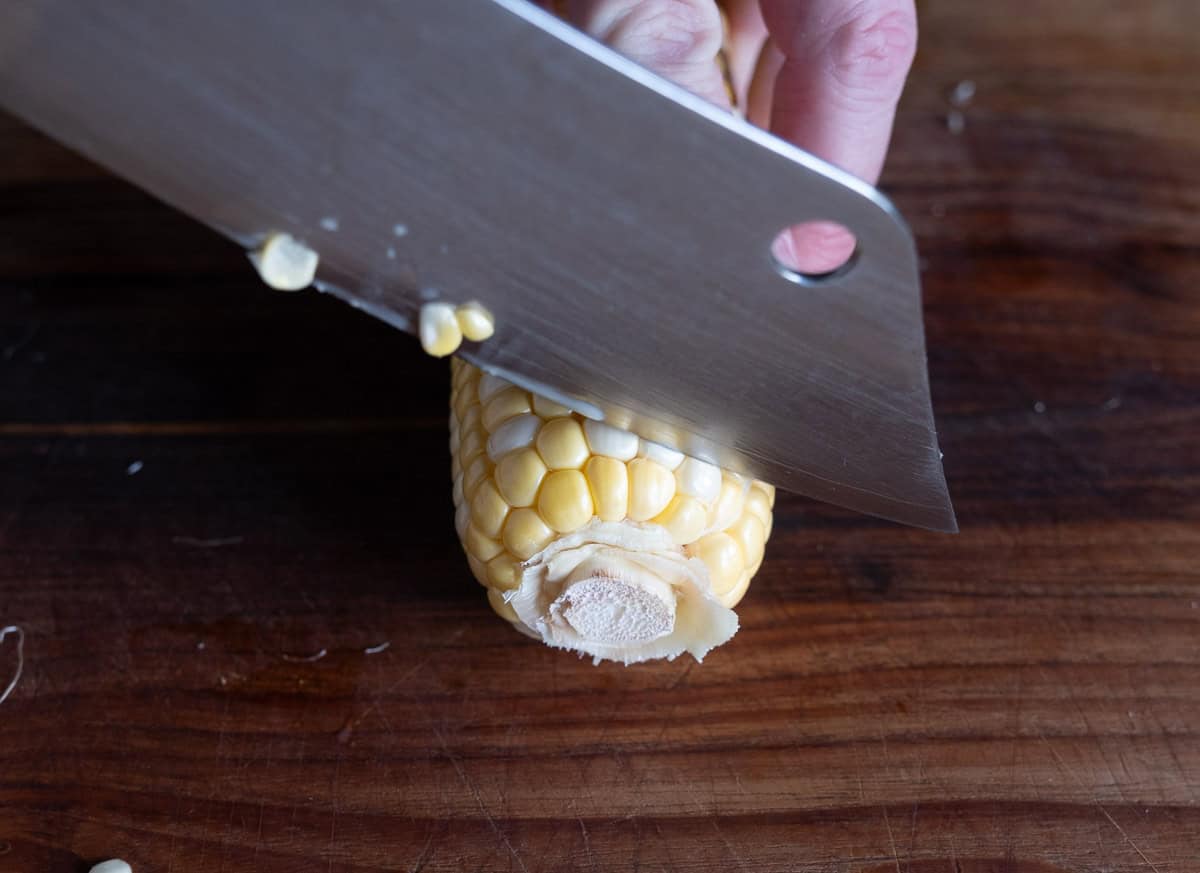 Removing the stem end of a corn cob with a sharp knife.