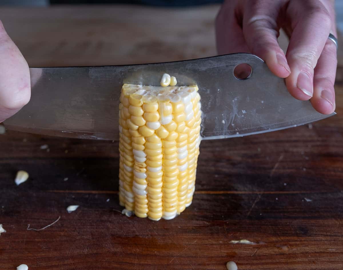 Standing up half of a corn cob and cutting in half.