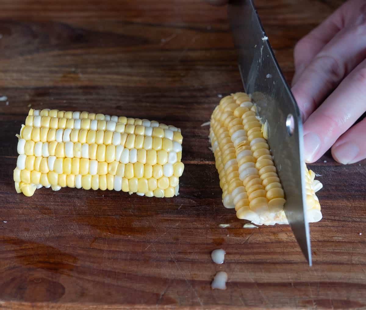 Cutting corn halves into quarters on a cutting board.