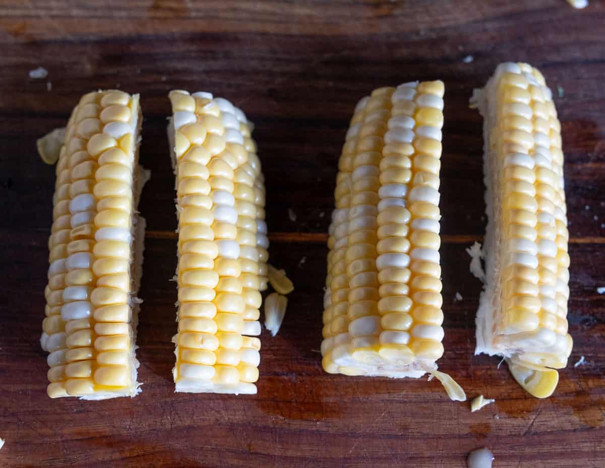 Quartered corn cobs in preparation for corn ribs on a cutting board.