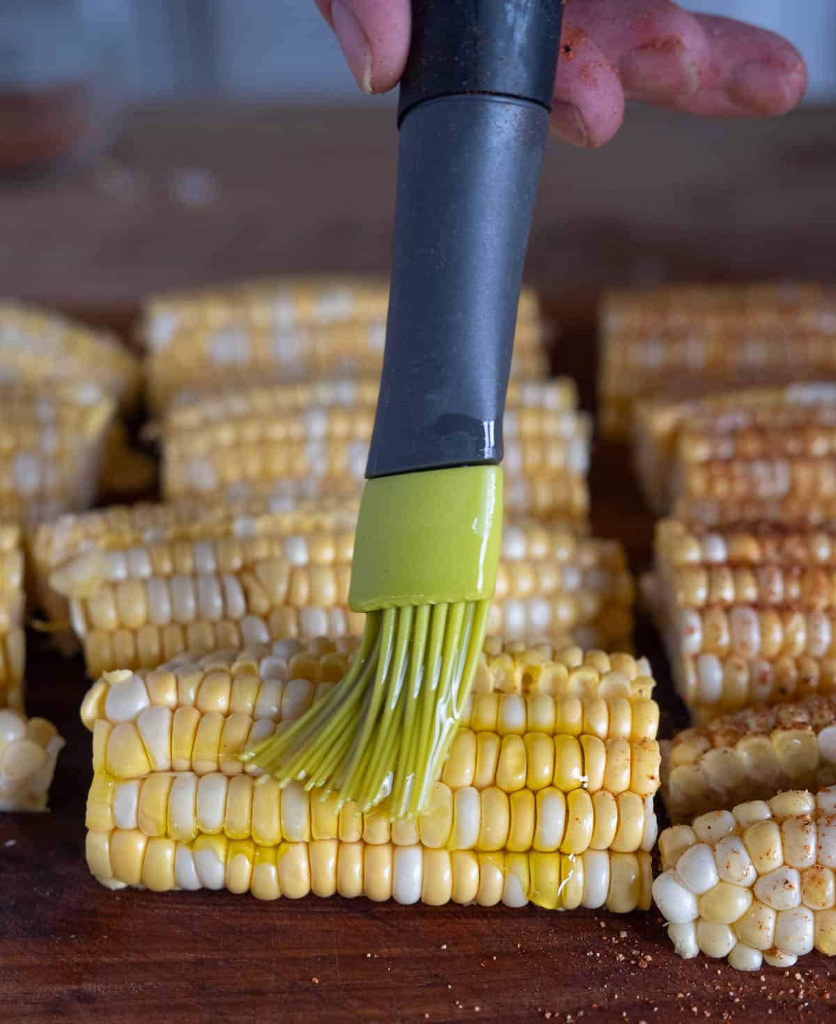 Brushing olive oil over prepared corn.