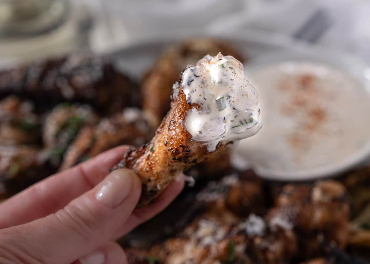 Mary from Vindulge holding a Parmesan garlic wing with some ranch on it over a plate of wings.