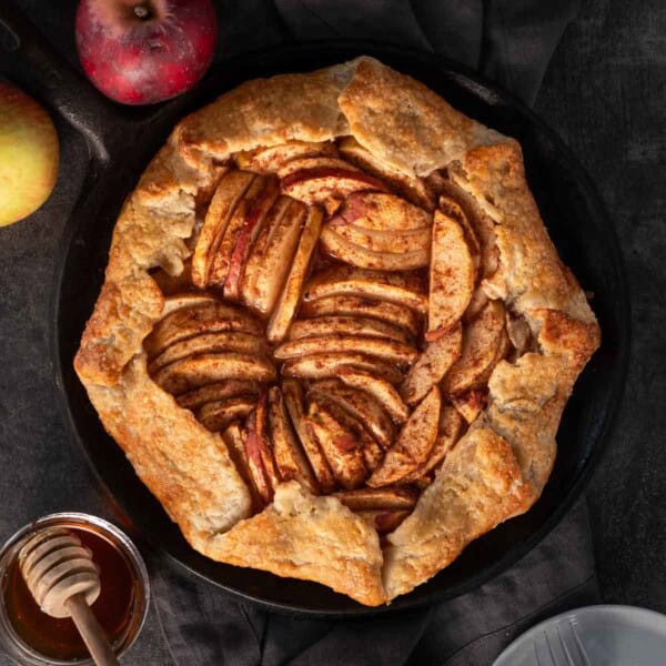 Grilled apple galette on a plate surrounded by apples.