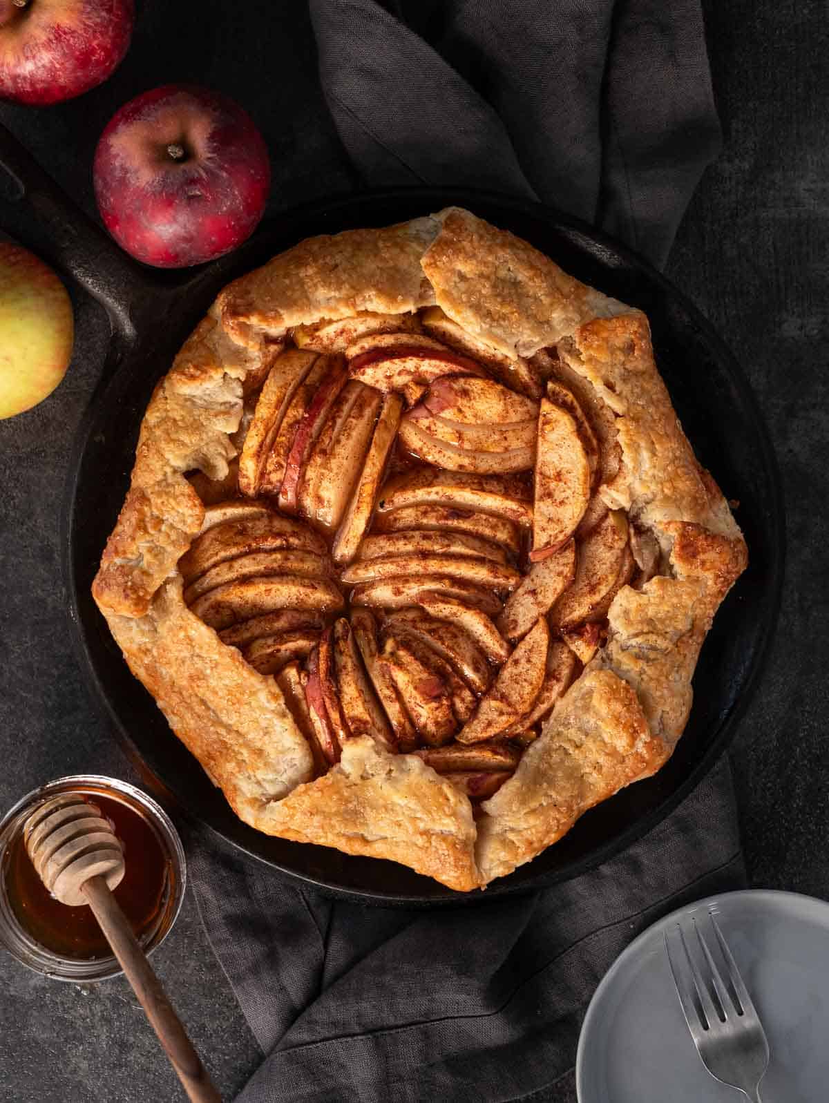 A grilled apple galette on a plate surrounded by apples.