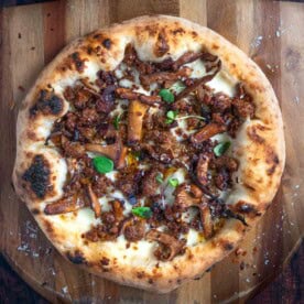 A sausage and chanterelle mushroom pizza on a cutting board