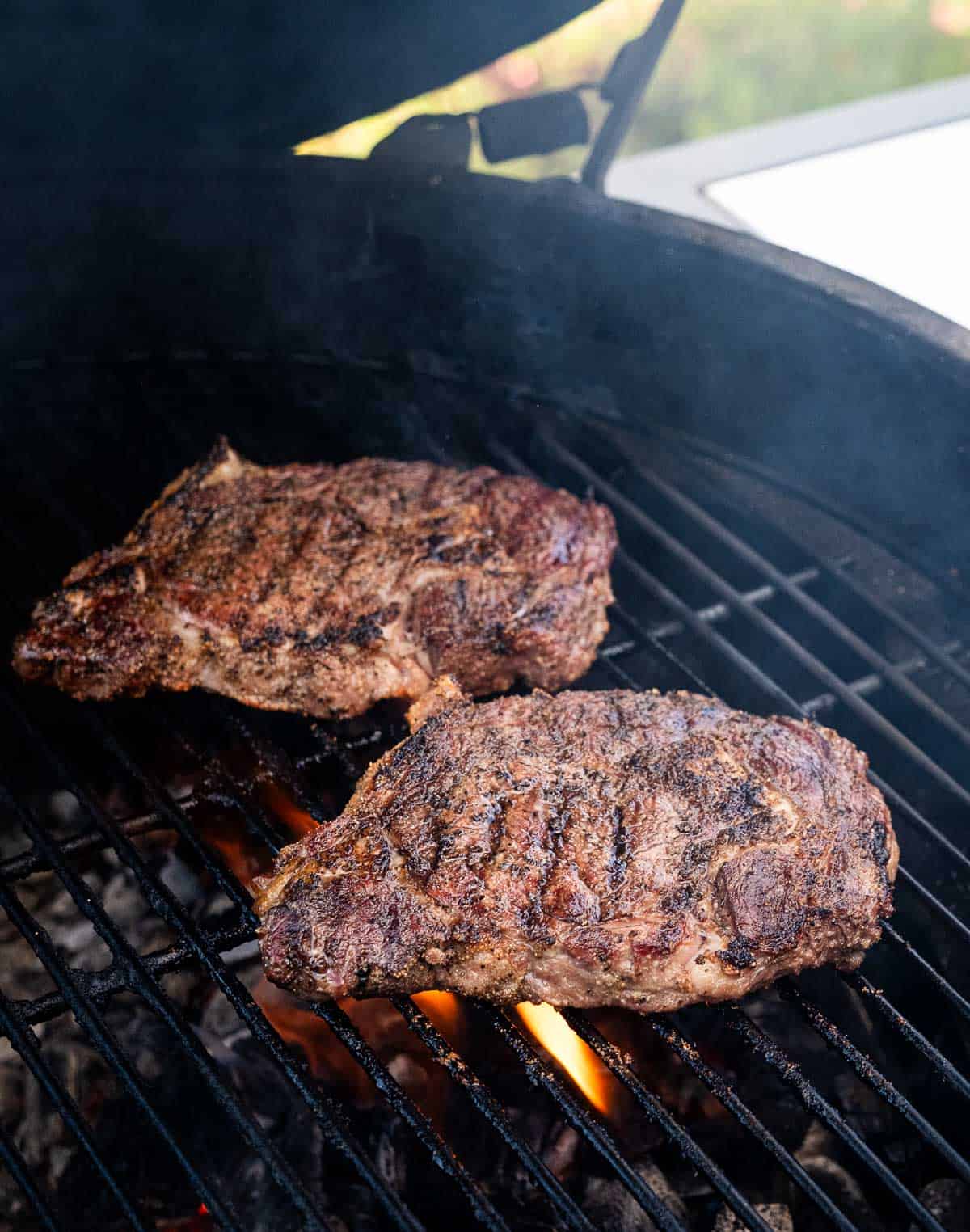 Two steaks on a grill side by side over direct heat.