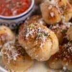 Garlic knots topped with cheese on a plate with marinara sauce.