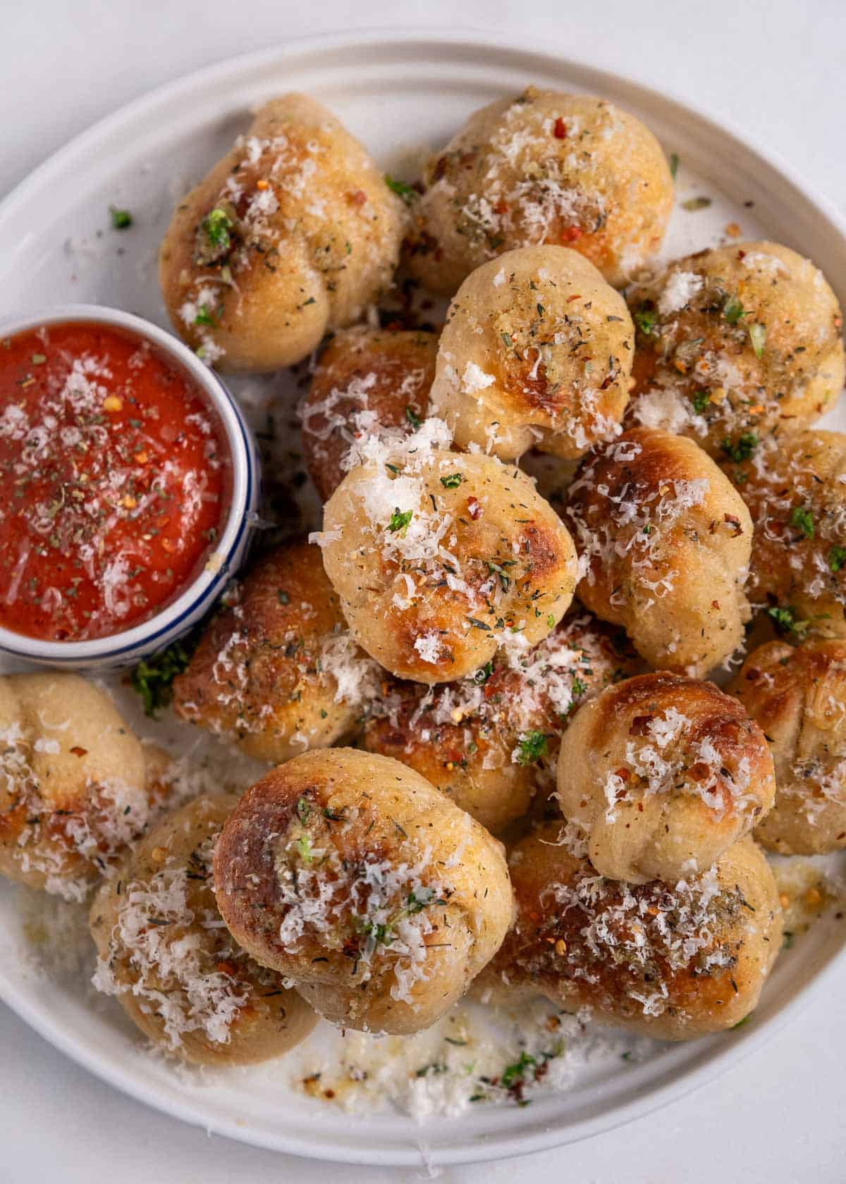 Homemade garlic knots on a serving dish with a side of marinara sauce