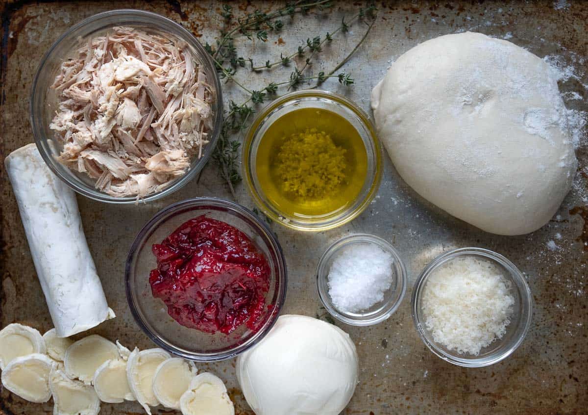 Ingredient photo for turkey pizza including dough, shredded turkey, and other ingredients in glass bowls.