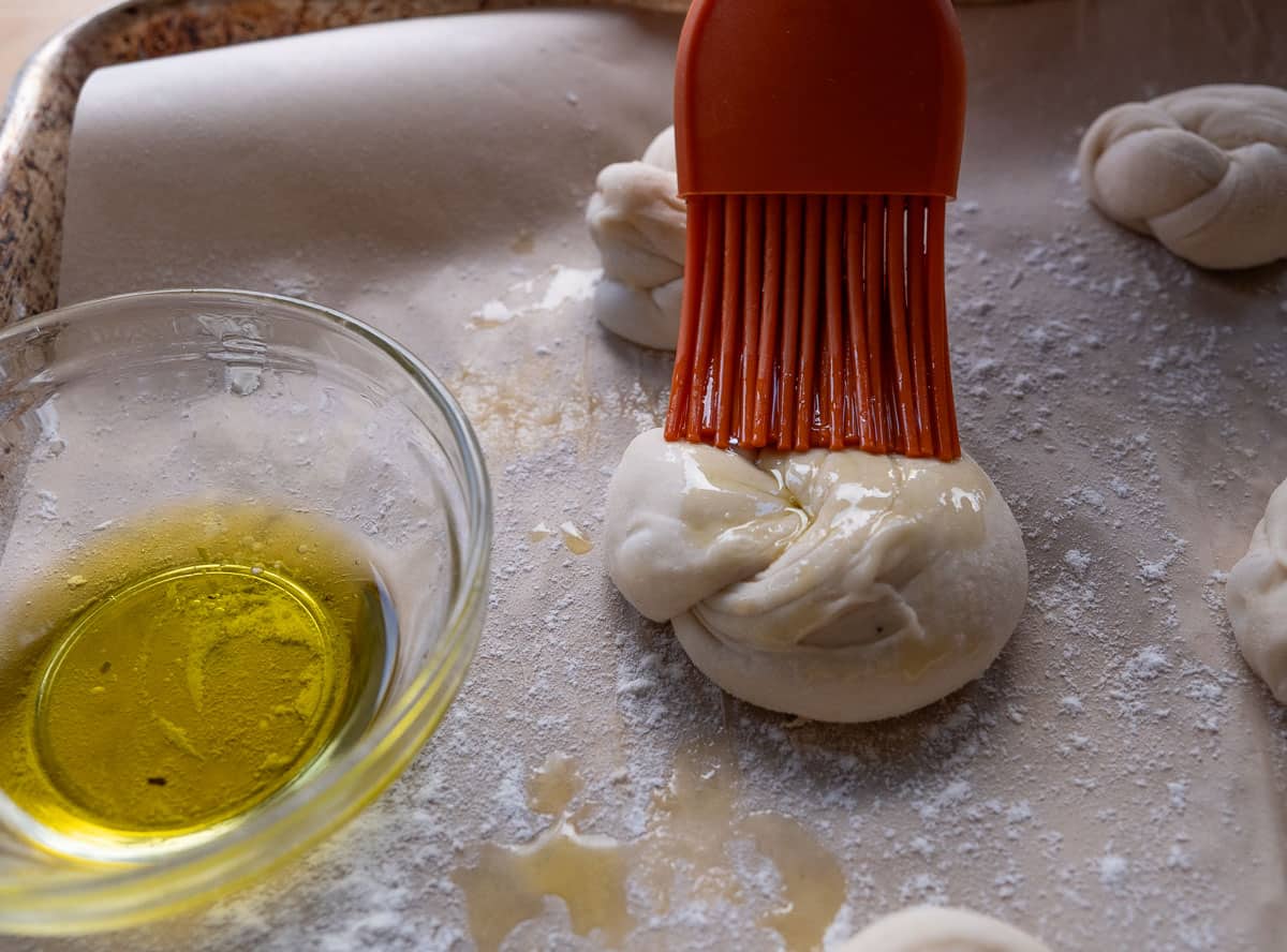 olive oil getting brushed onto an unbaked garlic knot