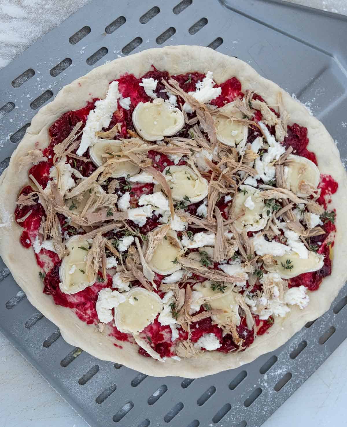 A pizza round with ingredients for turkey pizza before it has been cooked on a pizza peel.