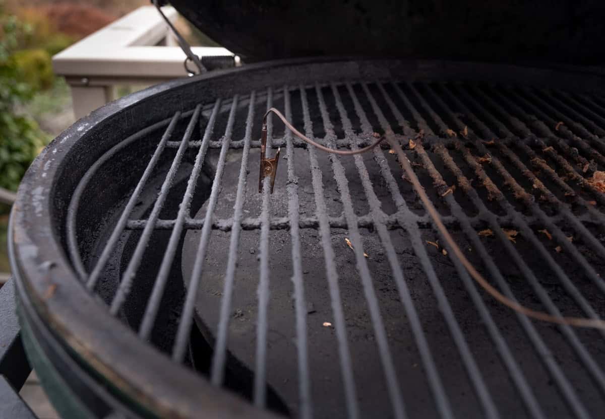 An image of the alligator clip for the Big Green Egg Genius clipped onto a grill grate over the conveggtor plate.