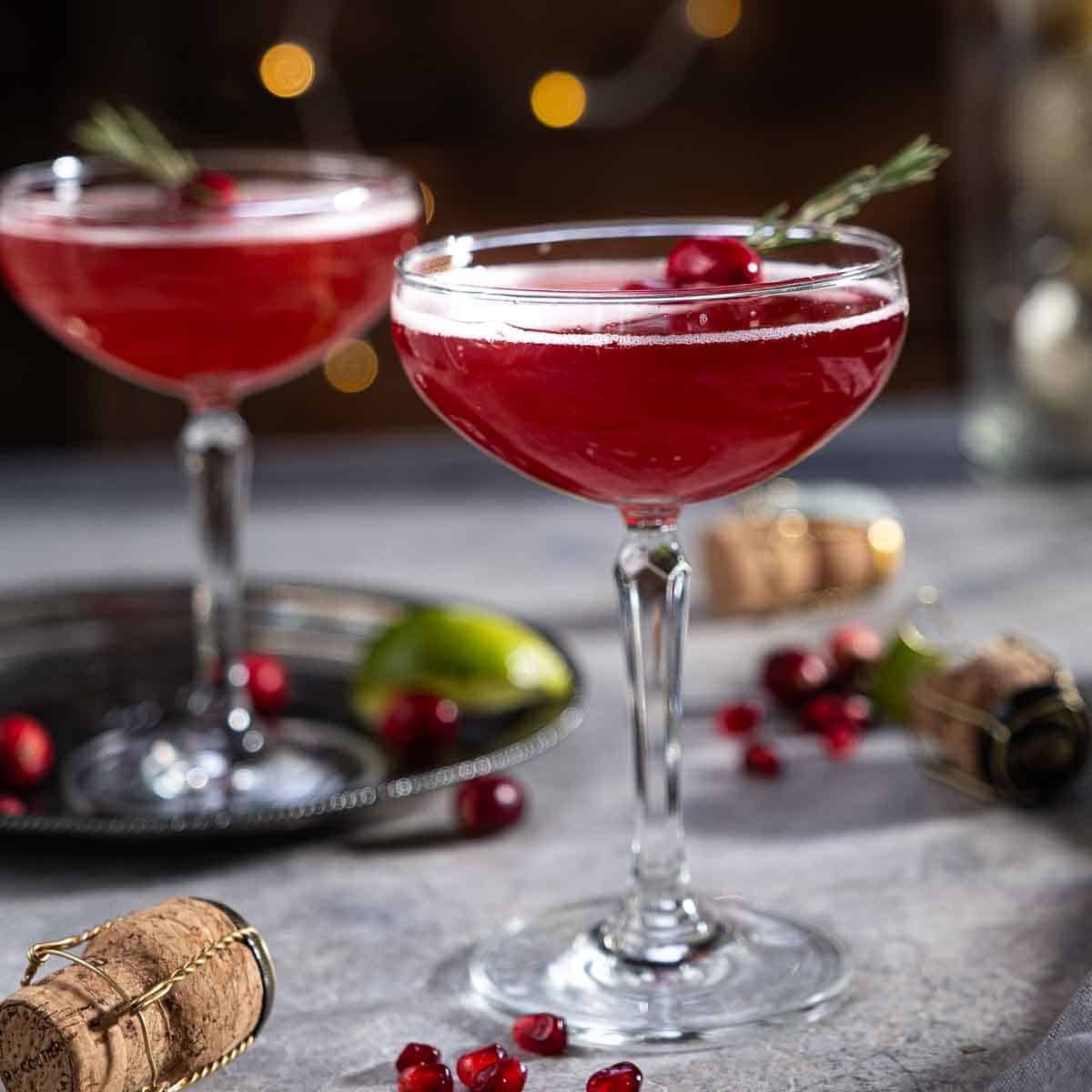 Two Christmas Mimosas on a table topped with cranberries and rosemary for garnish