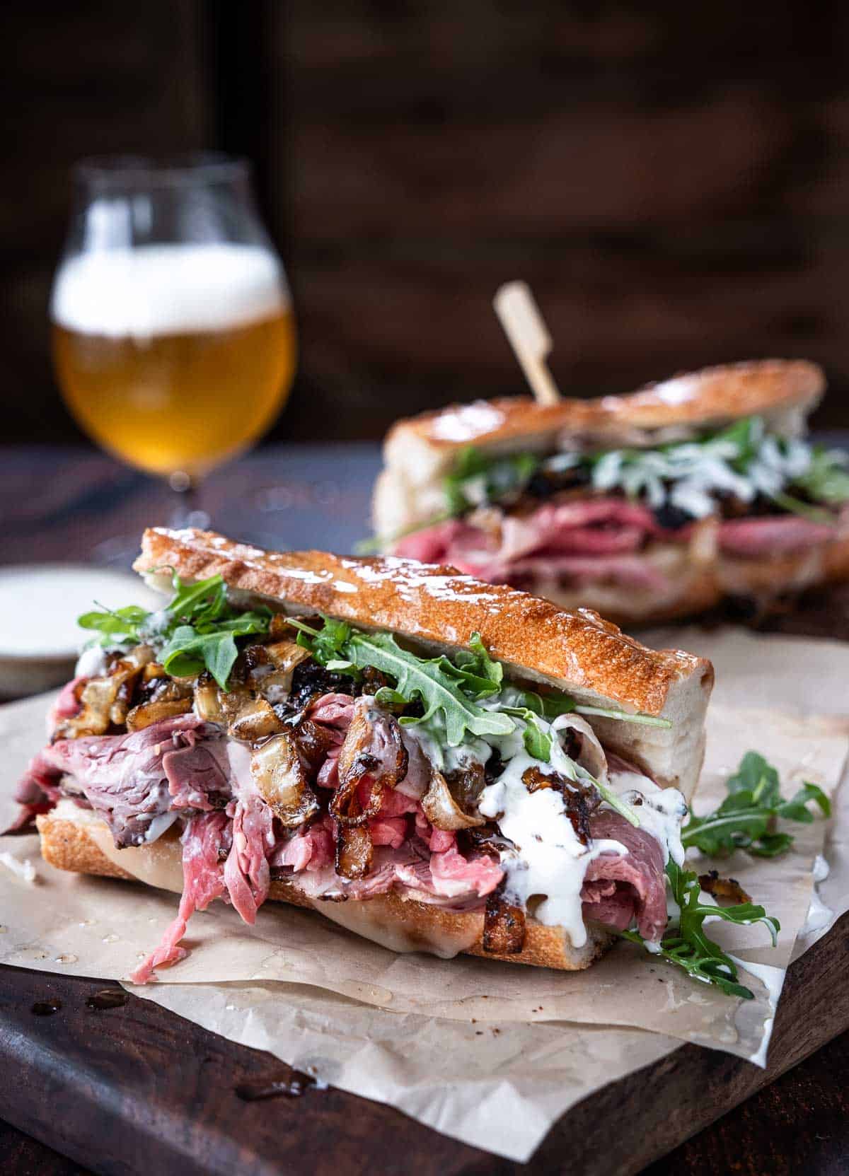 Prime Rib Steak Sandwiches on parchment paper on a cutting board with a beer.