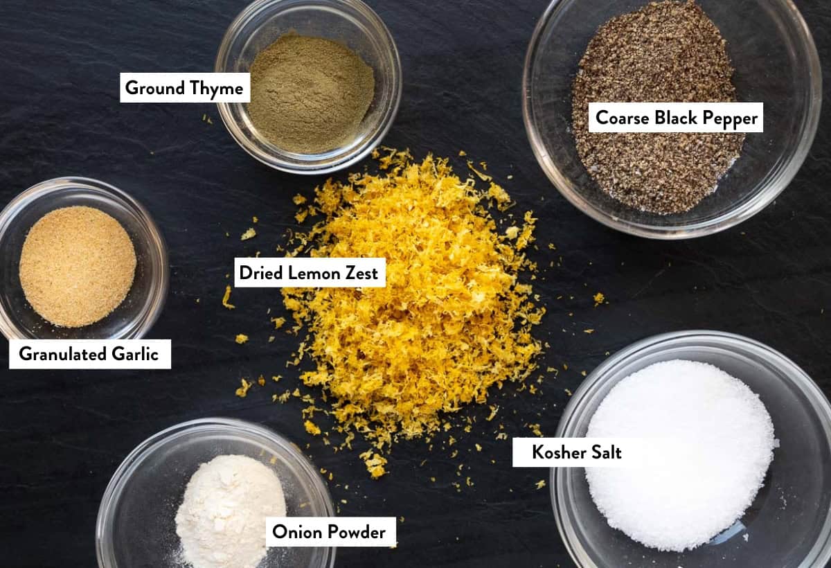 Ingredients for homemade lemon pepper seasoning on a black platter labeled with the names of the ingredients.