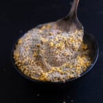 Lemon pepper seasoning in a small bowl with a spoon holding some of it up.