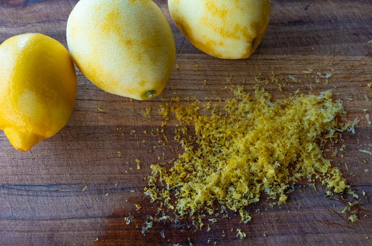 Three lemons on a cutting board with fresh lemon zest. 