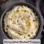 Creamy horseradish mashed potatoes in a grey bowl with a spoon topped with melted butter, chives, and cracked black pepper.