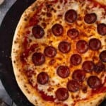 A sourdough pepperoni pizza using a sourdough pizza dough on a black plate.