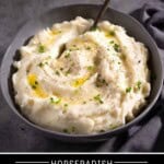 Creamy horseradish mashed potatoes in a grey bowl with a spoon topped with melted butter, chives, and cracked black pepper.