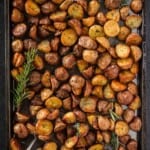 Breakfast potatoes with rosemary cut up and crispy in a sheet tray with small spatula.