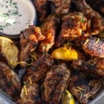 A plate of 16 lemon pepper wings with lemon wedges, zest, and a side of ranch.