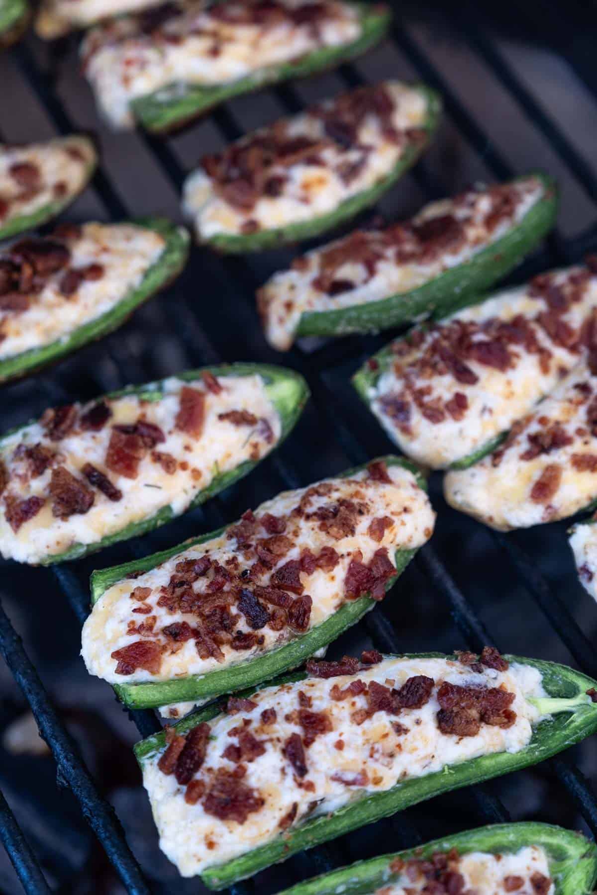 A jalapeño popper topped with crispy bacon cooking on the grill. 