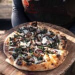 Mary from Vindulge holding a Kale and Mushroom pizza on a wooden cutting board.