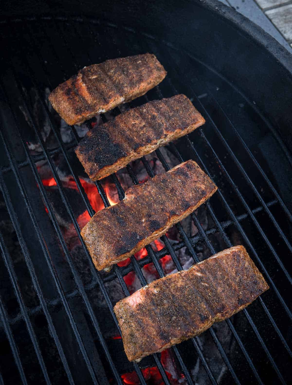 Four salmon steaks over direct heat on a grill seasoned with lemon pepper seasoning.