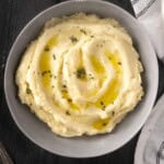 Parsnip puree in a bowl topped with melted butter and thyme on a wooden table.