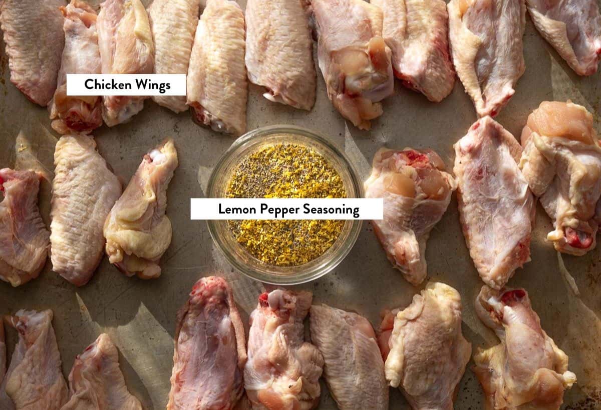 Raw chicken wings on a sheet pan with a bowl of homemade lemon pepper seasoning, labeled with ingredient names.