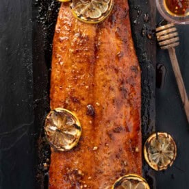 A Square image of hot honey salmon on a slate plate glazed with hot honey and topped with grilled lemons.