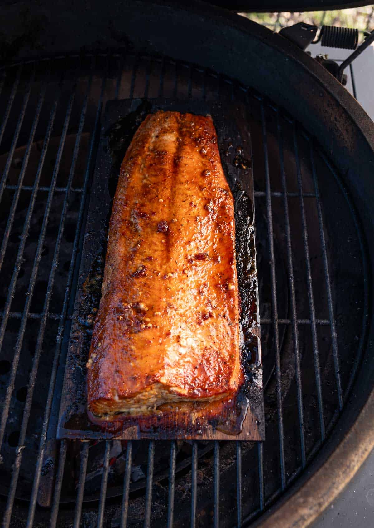 Hot Honey Salmon cooking on a cedar plank on the grill over direct heat.