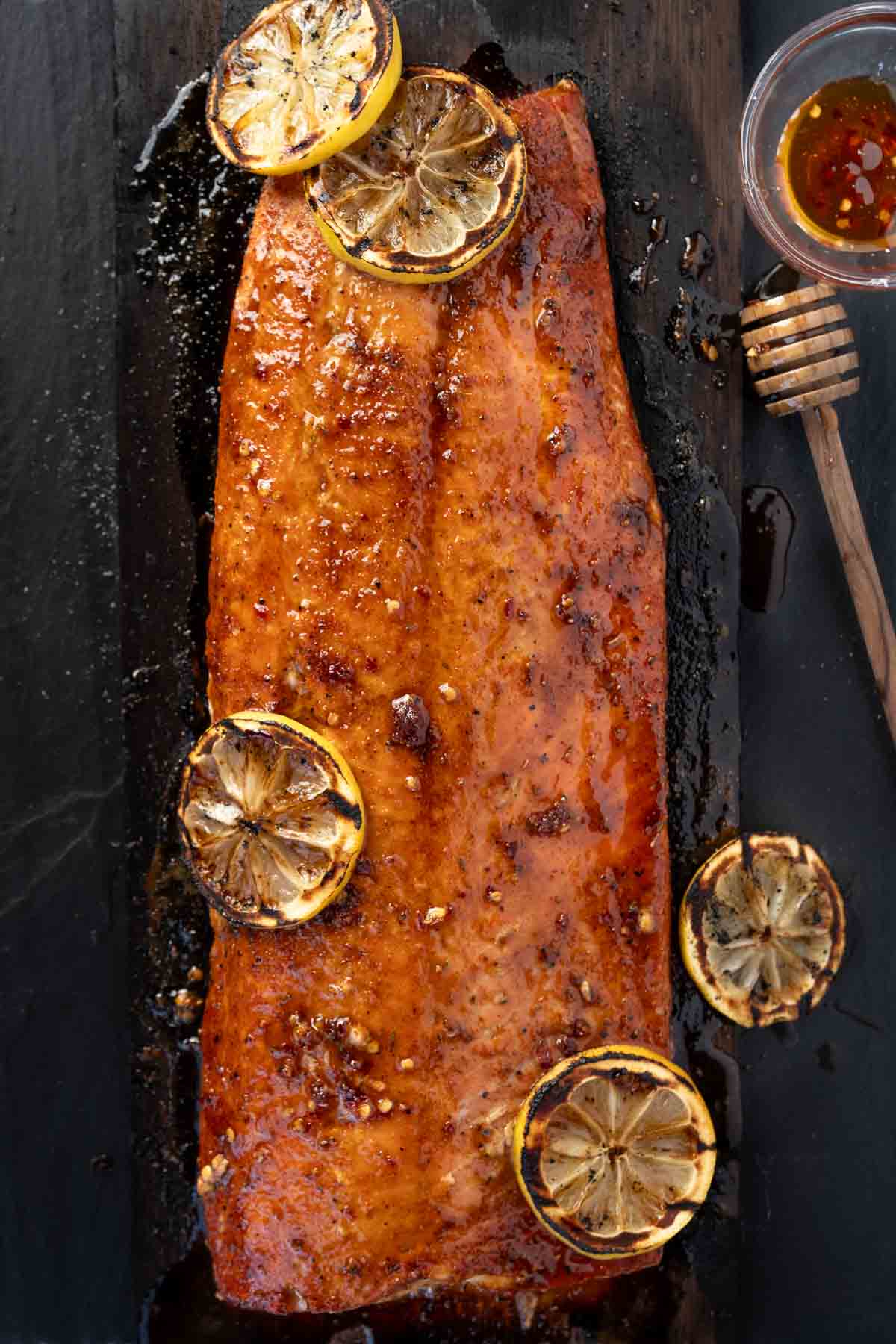 Grilled Hot Honey Salmon resting on a cedar plank with sliced of lemon on top.