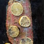 A grilled salmon filet covered in lemons with a garlic lemon paste glaze.