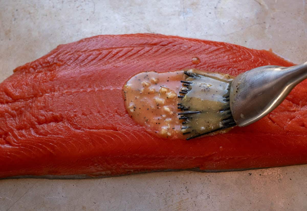 Raw salmon being brushed with a lemon garlic honey paste..